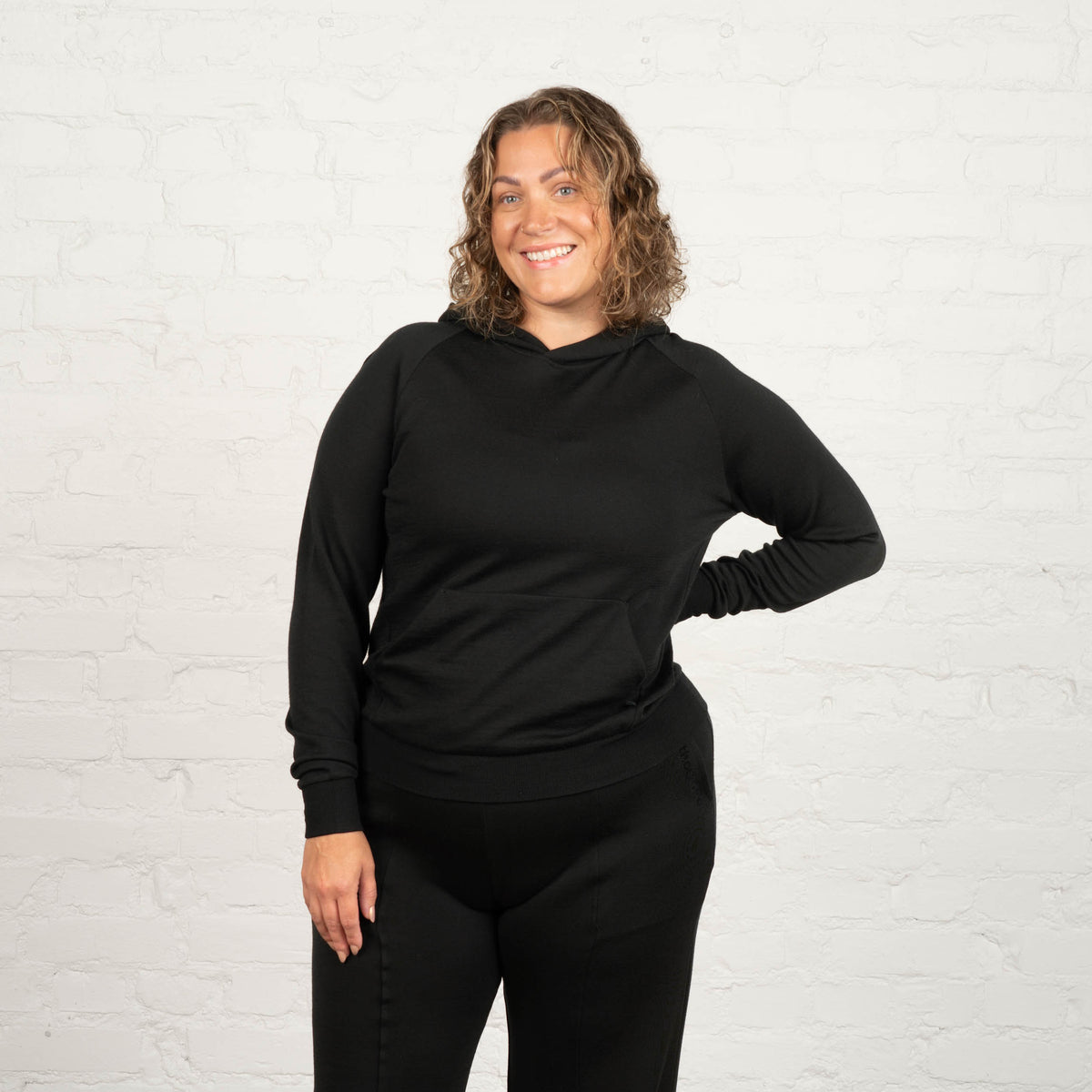 North Outdoor All Damen-Merino-Hoodie in Schwarz, mulesingfreie Merinowolle. Entworfen in Finnland - Model ist 178 cm groß und trägt Größe 2XL